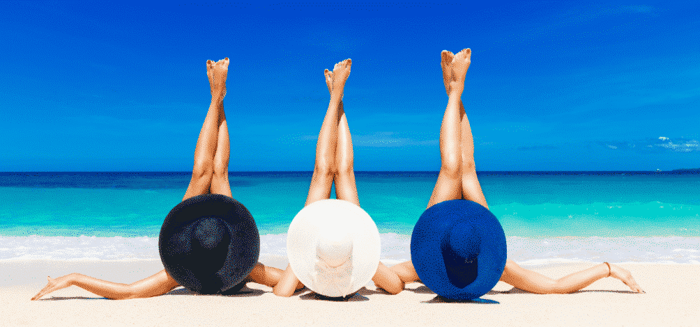 three women wearing sunhats lying down in the beach with their legs crossed up