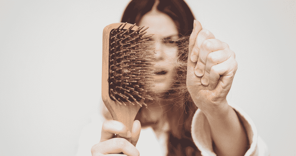 surprised woman in a bathrobe pulling hair out of a wooden hair brush