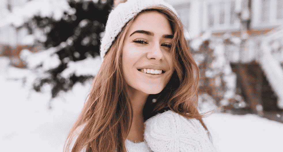 smiling brunnete woman in a white beanie standing outside in the snow