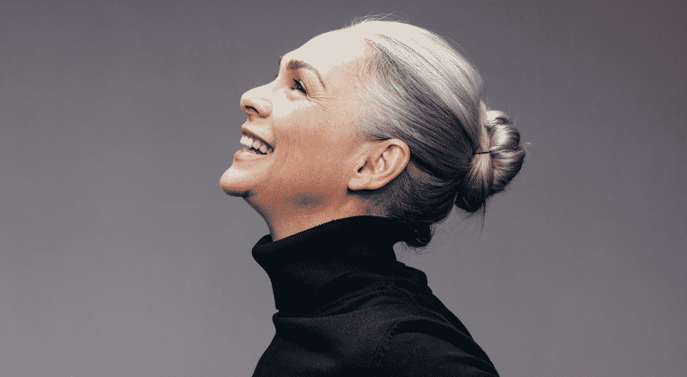 older woman with grey hair tied in a bun laughing while looking up